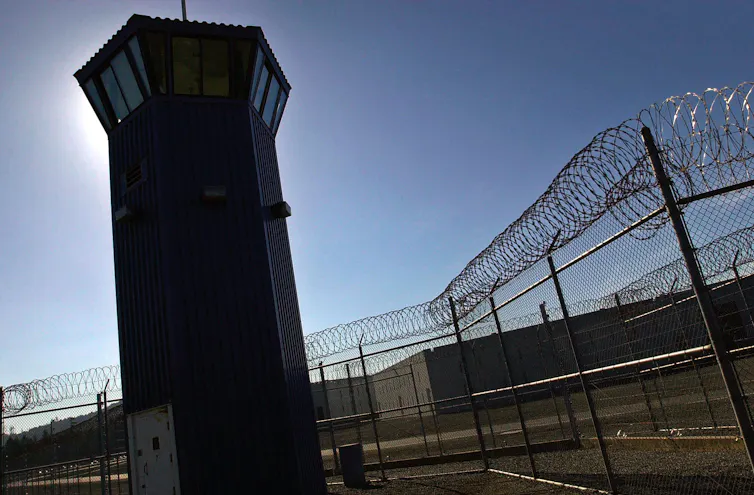 A prison watch tower beside a barbed wire fence.