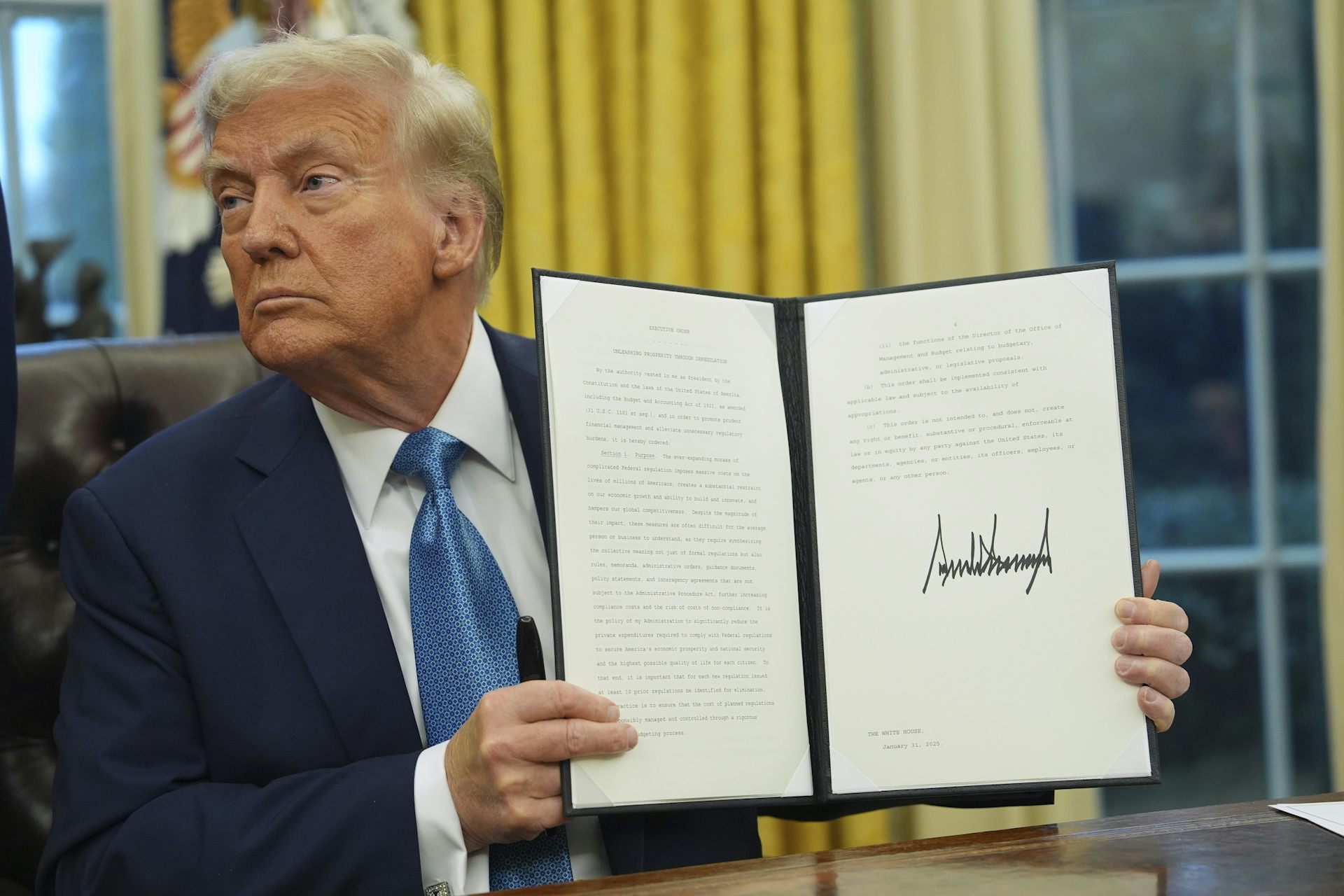 An elderly man with greyish-blond hair holds up a signed document.