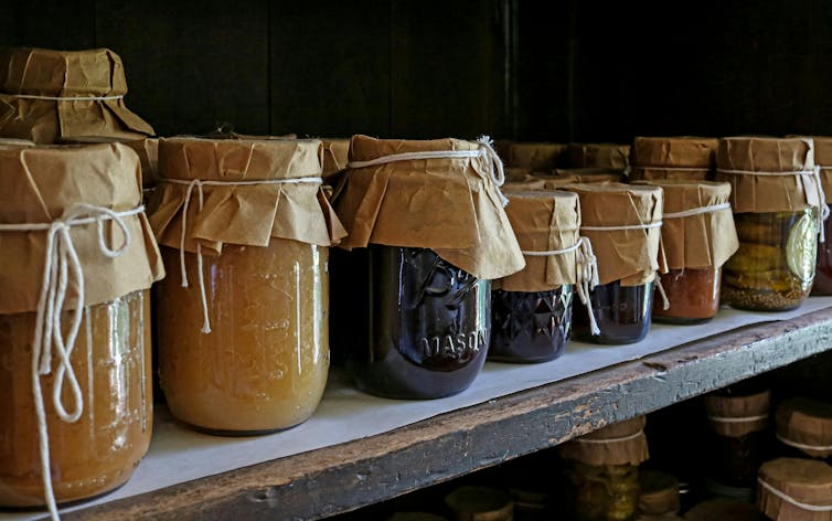 Mason jars containing home-made foods lined up on a shelf.