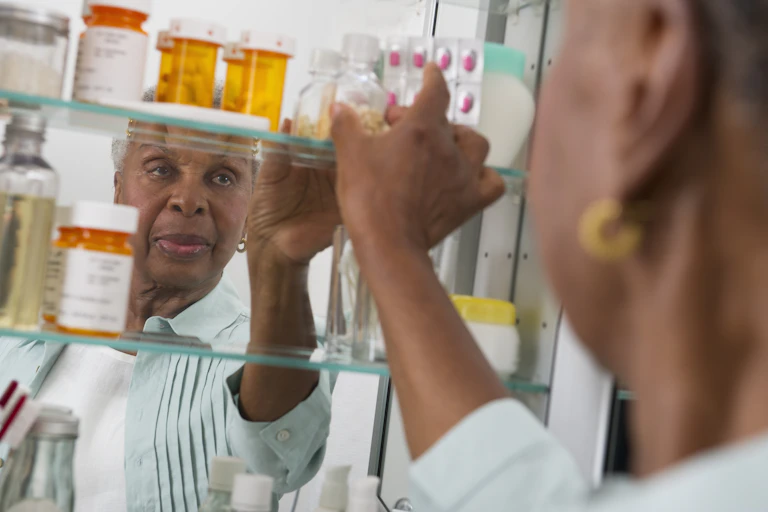 A woman reaches for a bottle in her medicine cabinet, which contains bottles and blister packs of medication