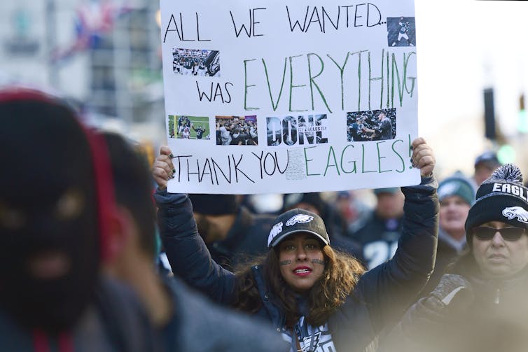 Woman in crowd on street holds sign that reads: 'All we wanted was everything. Thank you Eagles!'