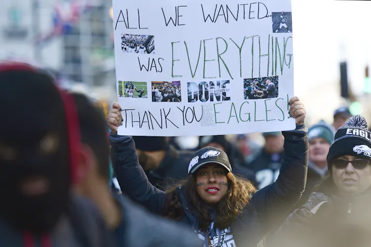 Woman in crowd on street holds sign that reads: 'All we wanted was everything. Thank you Eagles!'