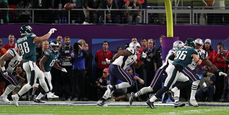 Football players compete on a field with people standing on sidelines