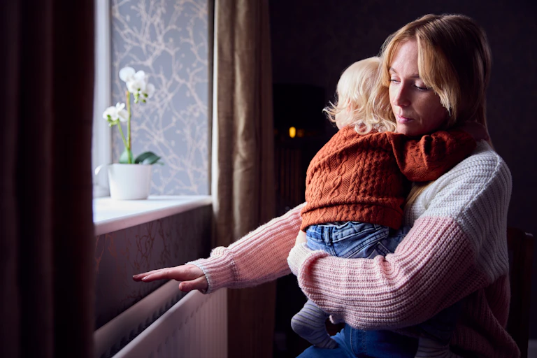 A young mother holding a child holds her hand above a radiator