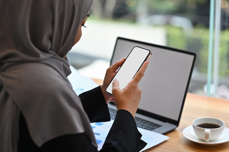 south asian woman in headscarf with a laptop and mobile phone