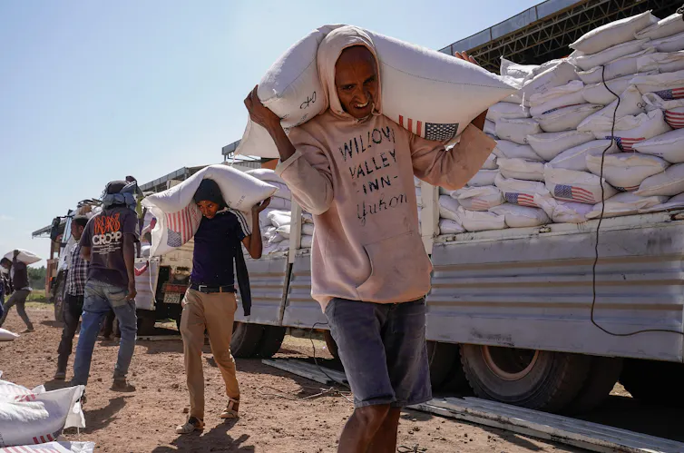Men carrying large sacks stand in front of a truck.