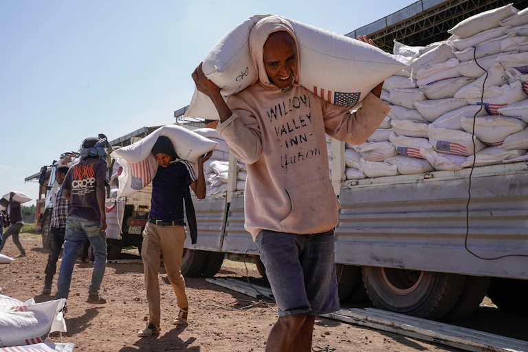 Men carrying large sacks stand in front of a truck.