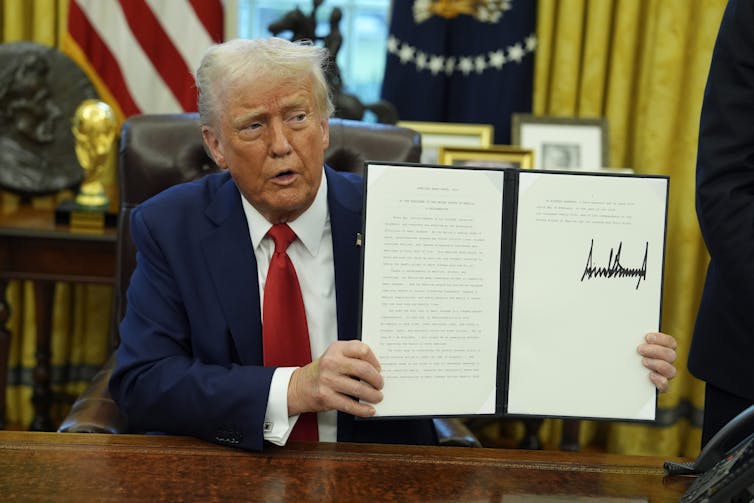 Caucasian man with orange skin and white hair lifts signed portfolio