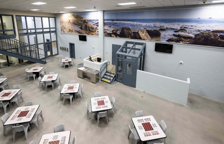 Murals are on the wall in a prison unit with patterned tables.