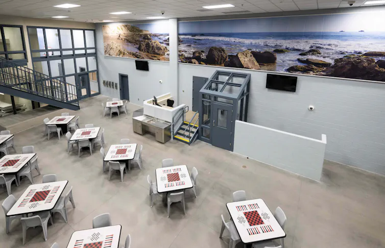 Murals are on the wall in a prison unit with patterned tables.