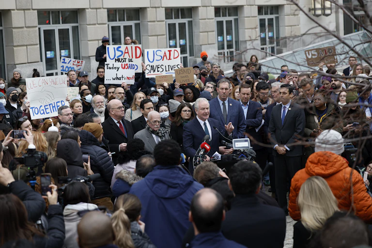 Crowd of people, some holding signs saying 'USAID saves lives.'
