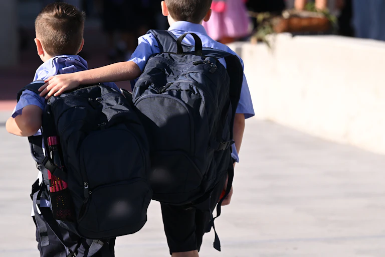 Two young students with backpacks walk along. One has an arm around the other.