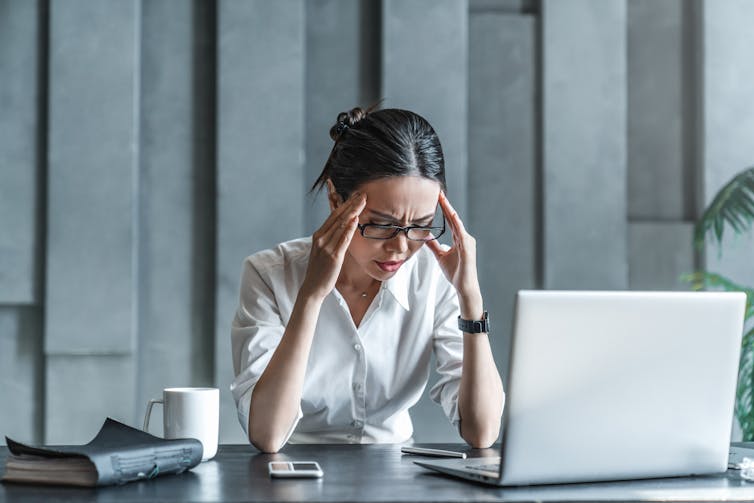 A woman with a grimace on her fact rests her fingers against the sides of her head