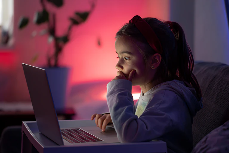 Young girl sitting on a couch, looking at a computer.