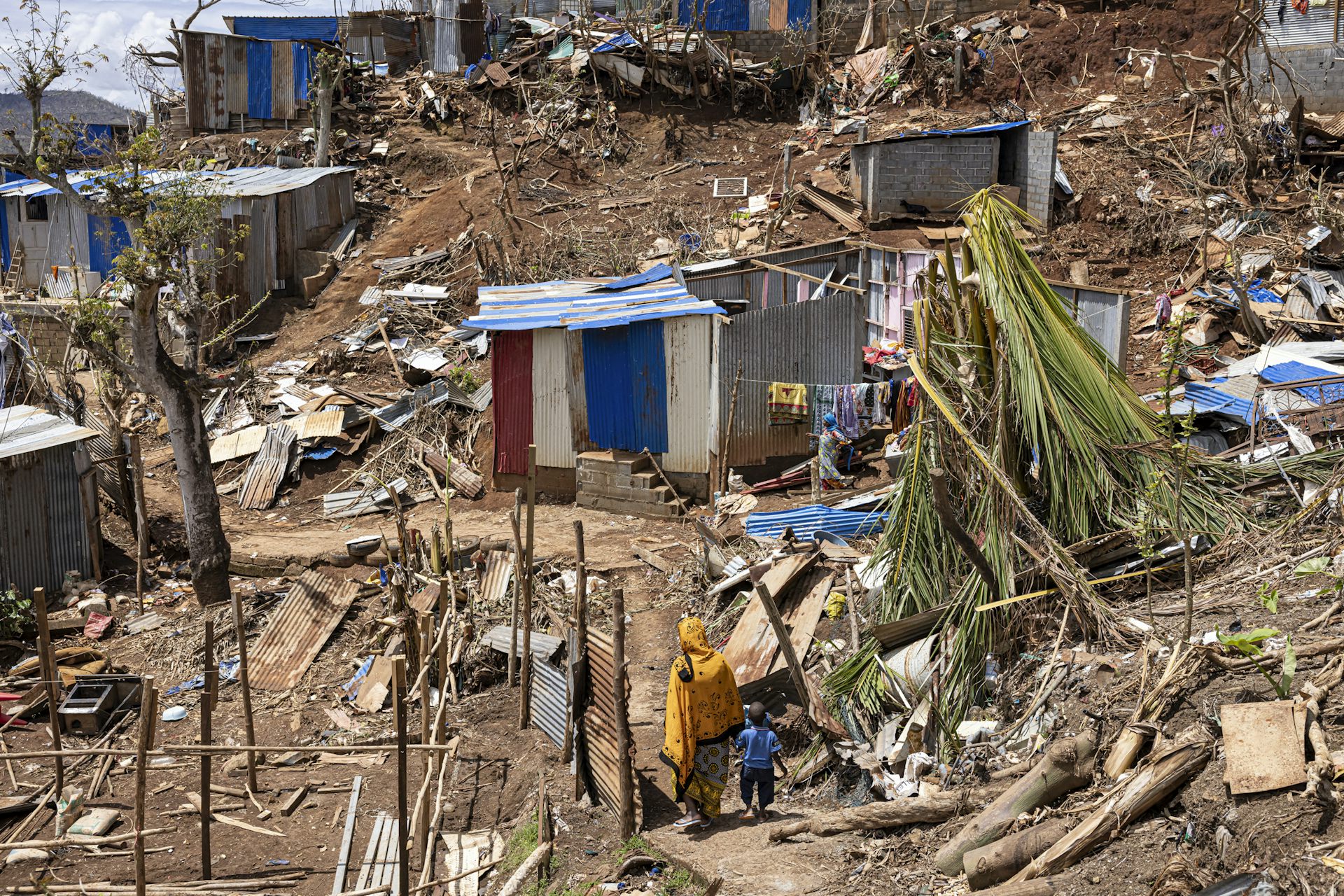 Image d'une femme et son enfant marchent parmi les débris dans la ville de Vahibe, à la périphérie de Mamoudzou, à Mayotte, le 24 décembre 2024, une semaine après le passage du cyclone Chido sur l'archipel. 