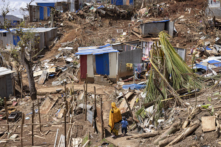 Image d'une femme et son enfant marchent parmi les débris dans la ville de Vahibe, à la périphérie de Mamoudzou, à Mayotte, le 24 décembre 2024, une semaine après le passage du cyclone Chido sur l'archipel.