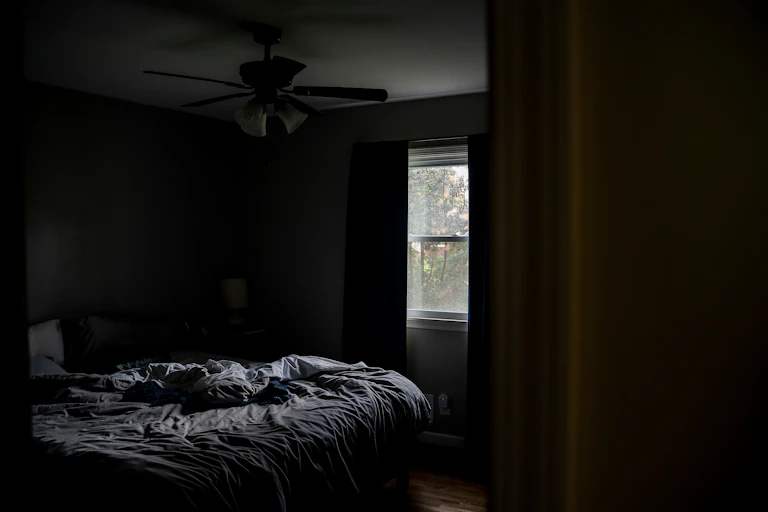 A unmade bed in a dark room.