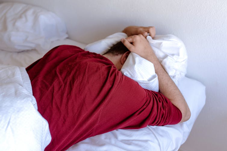 A man in bed buries his head in his pillows.