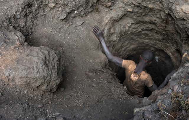 An African man descends a hole in the ground, seen from above.