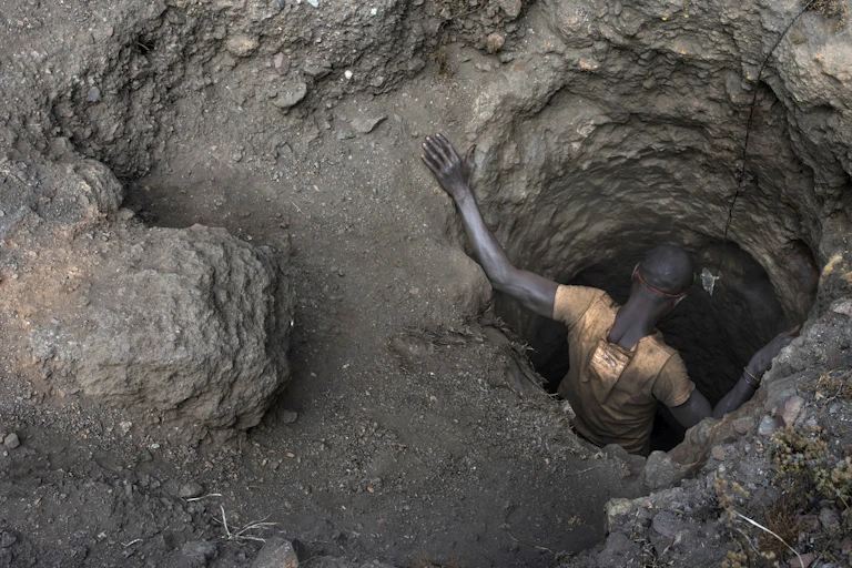 An African man descends a hole in the ground, seen from above.