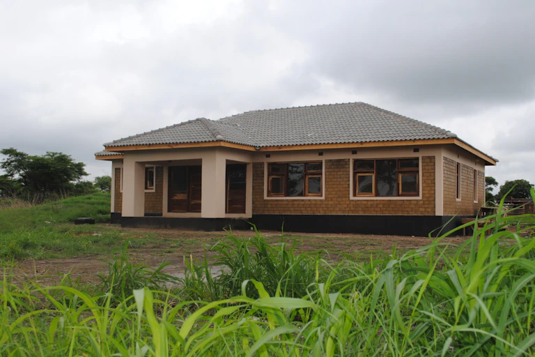 A roomy brick house with wooden windows stands in an open area with grass and trees