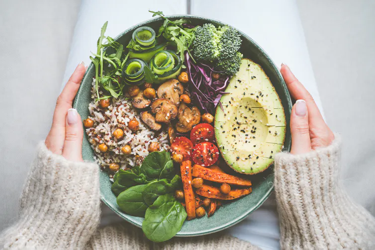 A woman's hands hold a bowl containing a plant-based meal.