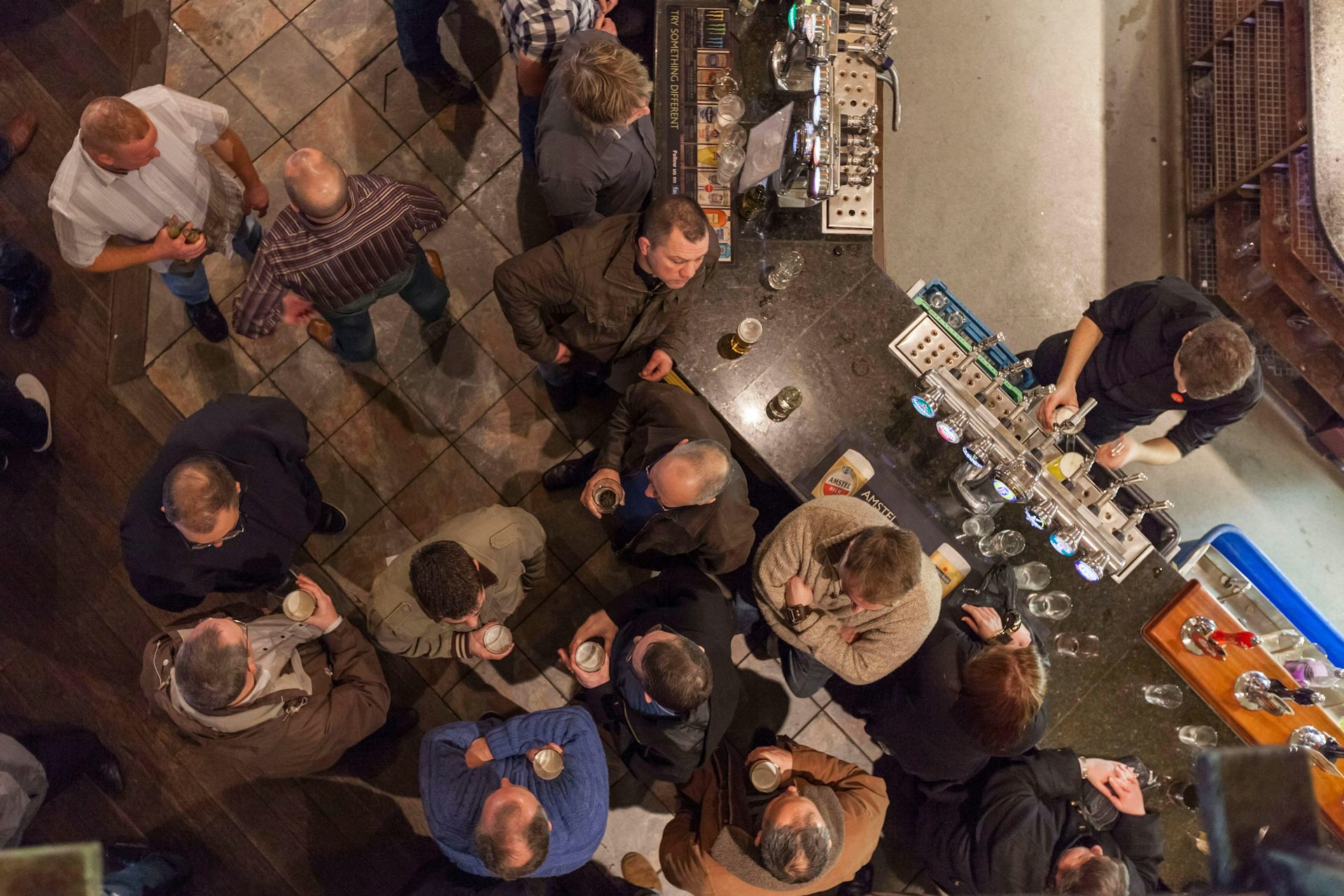 A bird's eye view of customers holding pints of beer in a pub.