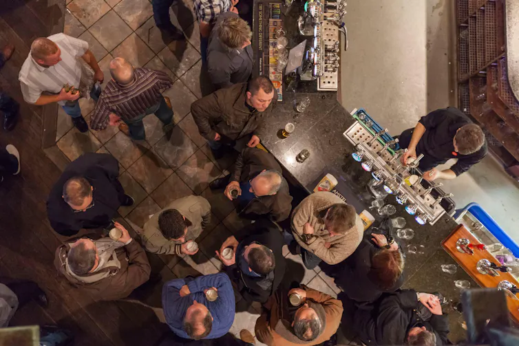 A bird's eye view of customers holding pints of beer in a pub.