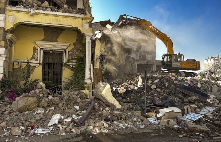 A construction digger demolishing the damaged remains of a building.