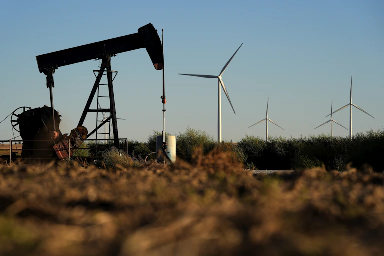 A pumpjack seen in a field with four windmills in the distance