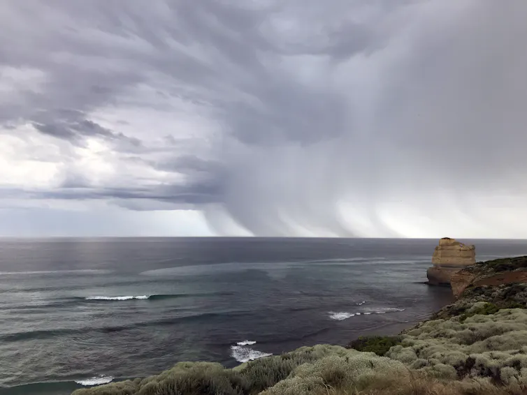 View from a clifftop, looking out at a rain storm over a calm ocean.