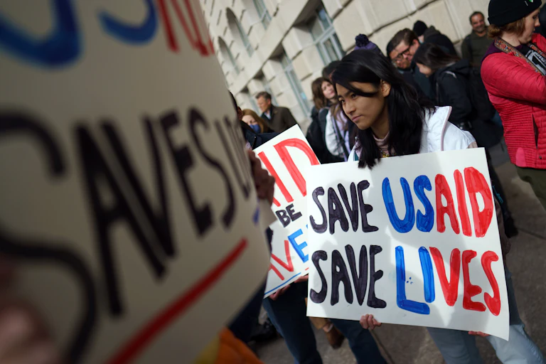 A woman holds a sign that says save USAID save lives