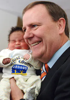 Peter Costello holds a young baby in a hospital