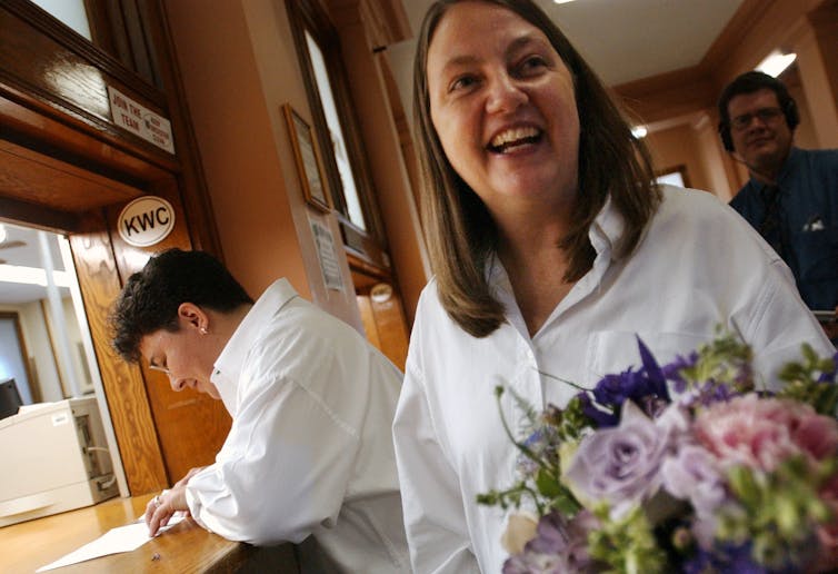 A woman fills out a marriage license as her partner holds a bouquet.