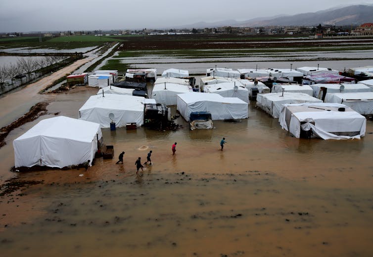 Syrian refugees make their way in flooded water at a temporary refugee camp, in the eastern Lebanese Town of Al-Faour near the border with Syria, Lebanon