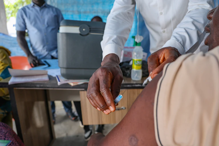 A man about to inject another man while others look on.