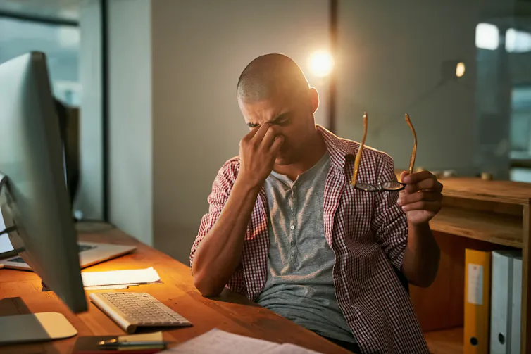 Man pinching nose in front of computer