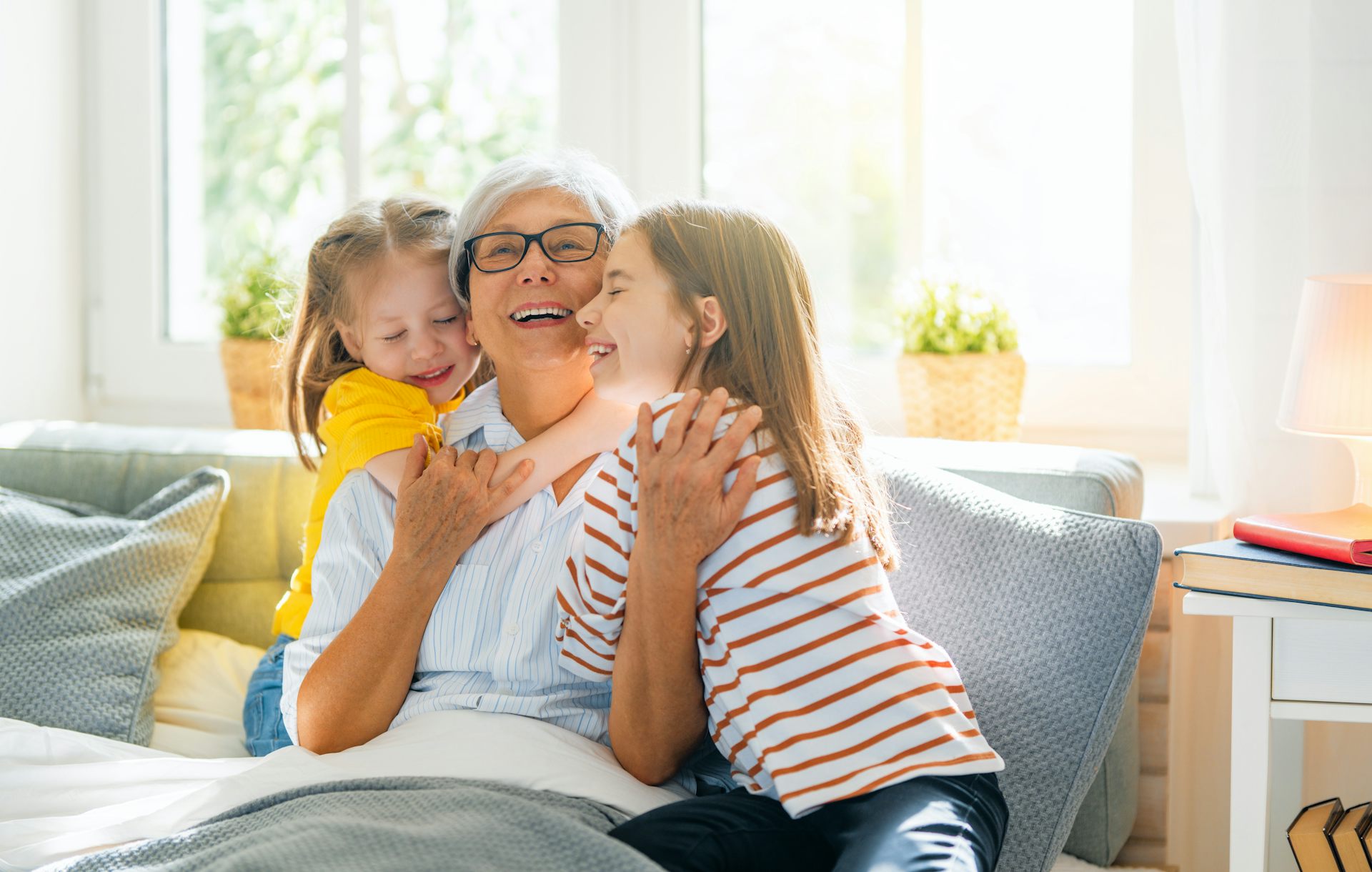 une femme aux cheveux gris assise sur un sofa et encadrée par deux petites filles