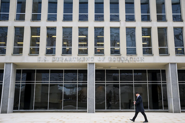 A person walks by a large building that says 'U.S. Department of Education' on it