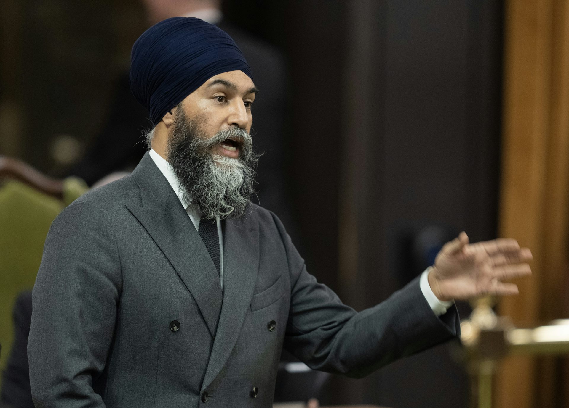 Un homme portant un turban et un veston cravate est debout et parle avec le bras levé