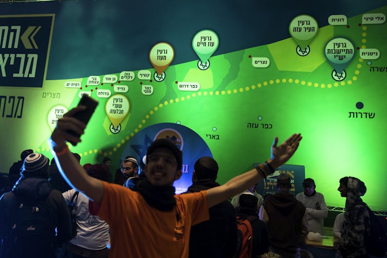 A man with a cell phone stands in front of a big green map.