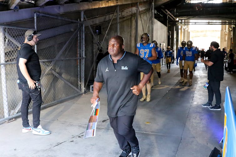 A Black man is jogging through a tunnel onto a football field.
