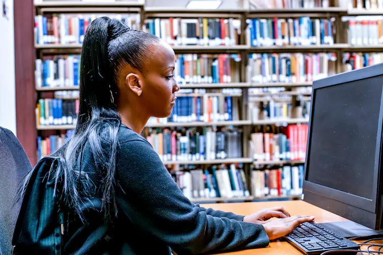 Young woman works at a computer with library stacks in the background