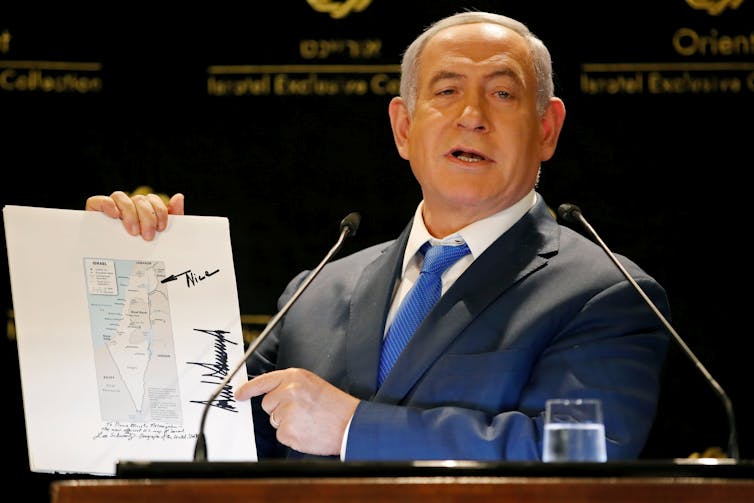 A man in a suit and blue tie holds a map.