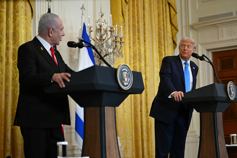 Two men in suits stand at podiums talking to each other.
