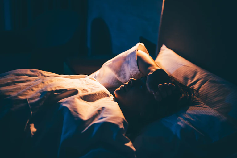 Person in bed unable to sleep, arm thrown over face