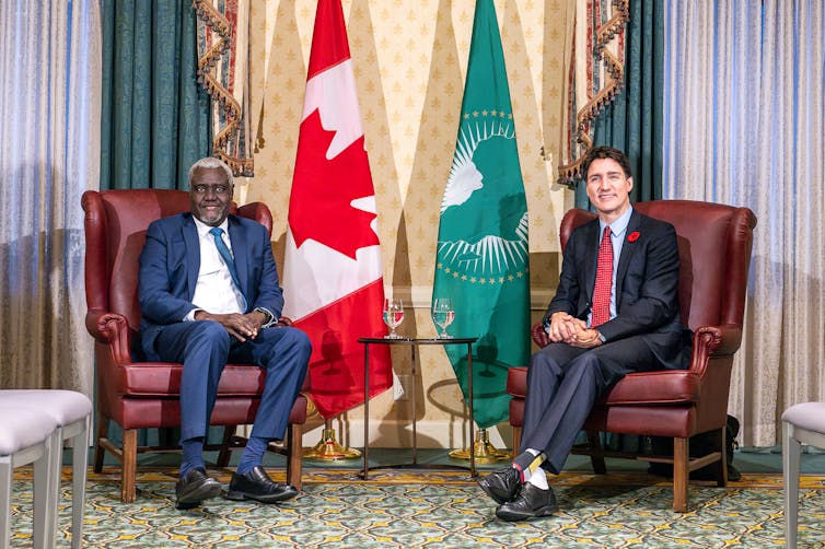 El hombre blanco y el hombre negro sonríen mientras están sentados en sillas de cuero frente a la comunidad canadiense y africana.