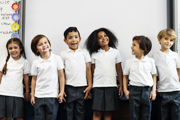 Young students in white shirts line up against a whiteboard.