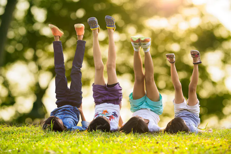 Four kids lie on the grass with their legs in the air.