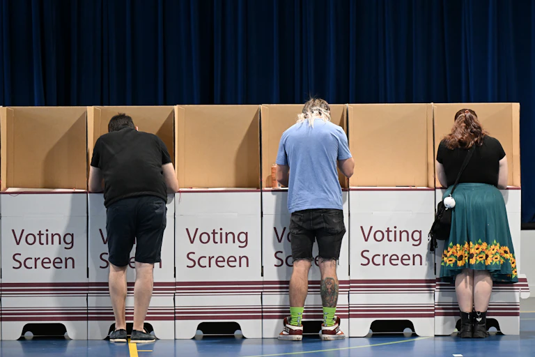 Three people casting their votes in an election booth
